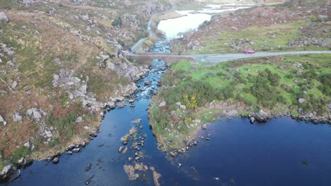 Wide-panning-aerial-shot-of-Gap-of-Dunloe,-Bearna-or-Choimín,-mountain-pass-in-County-Kerry,-Ireland,-with-a-bridge-over-the-river-Loe