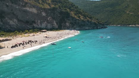 Low-aerial-overview-of-tourists-strolling-on-beautiful-sandy-beach-of-the-Albanian-Riviera