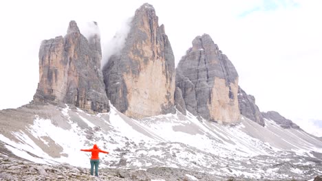 Rear-view-of-a-woman-in-an-orange-hoodie-raising-her-arms-after-reaching-the-snowy-slope-of-Tre-Cime-di-Lavaredo
