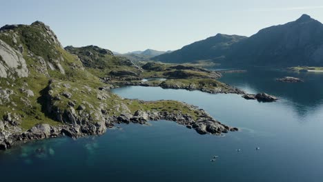 Aerial-drone-shot-of-scandinavian-landscape-with-group-of-paddle-boarders,-dramatic-mountains,-ocean-and-verdant-greenery