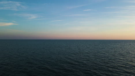 Gentle-soft-glow-of-sunrise-spreads-across-open-ocean-water-texture,-drone-dolly