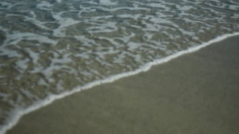 Ocean-water-lapping-against-sandy-beach,-mid-shot