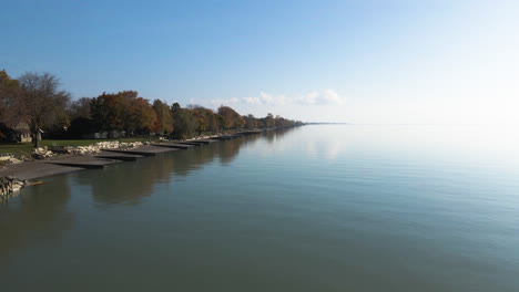 Aerial-dolly-along-peaceful-early-morning-lakeside-water-homes-and-erosion-control-barries-of-Lake-Erie