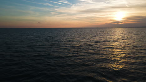 Sunset-glowing-light-reflects-dancing-across-ripples-in-ocean-water-below-clouds