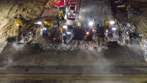 Excavators-with-various-tool-demolish-bridge-during-nighttime,-aerial