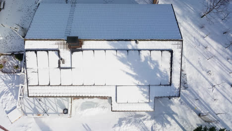 Birds-eye-drone-shot-over-snowy-solar-cells,-melting-on-a-sunlit-house-roof