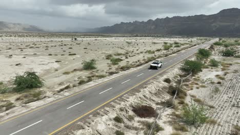 Aerial-drone-following-shot-over-a-car-driving-along-the-highway-road-through-Hingol-National-Park-in-Balochistan-on-a-cloudy-day