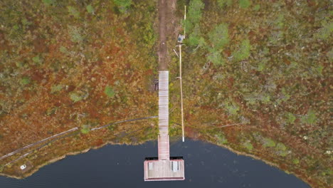 Bird's-Eye-View-Of-A-Wooden-Pier-On-Black-Lake-In-Autumn-Forest-Of-Sweden