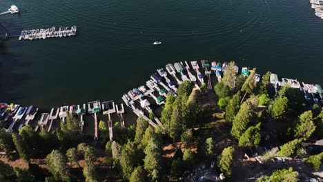 sun-setting-over-lake-arrowhead-village-and-marina-reveal-from-mountain-homes-to-the-lake-filled-with-boats-moving-fast-orange-colors-AERIAL-DOLLY-TILT-UP