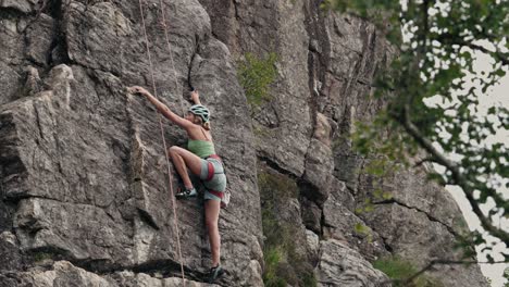 Young-woman-with-helmet-and-ropes-climbing-cliff,-side-view