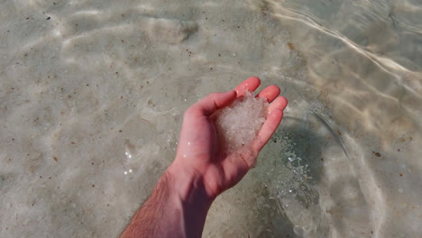 Male-hand-grabs-thick-silica-salty-sand-from-the-Dead-Sea-raises-to-view