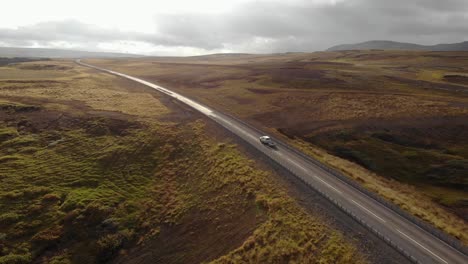 Coche-Blanco-Conduciendo-Por-Una-Carretera-En-Un-Amplio-Paisaje-Durante-La-Puesta-De-Sol-En-Islandia