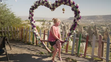 Woman-sits-on-heart-shape-floral-decorated-swing-love-valley-overlook