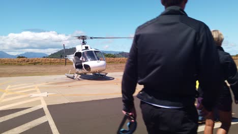 Gimbal-wide-shot-approaching-helicopter-on-foot-with-ground-control-and-passengers-at-a-heliport-in-Kaua'i,-Hawai'i