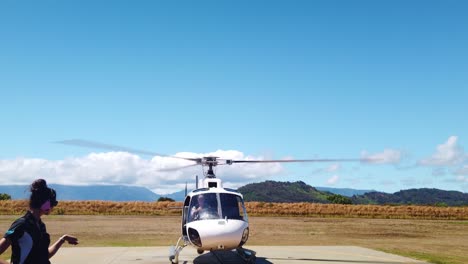 Gimbal-wide-booming-down-shot-of-a-helicopter-pilot-getting-signal-from-ground-control-to-begin-boarding-tourists-at-a-heliport-in-Kaua'i,-Hawai'i