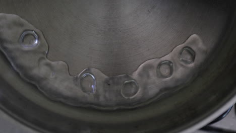 Slow-Motion-view-capturing-the-moment-water-splashes-into-a-hot-stainless-steel-pan,-connecting-in-a-semi-circular-motion