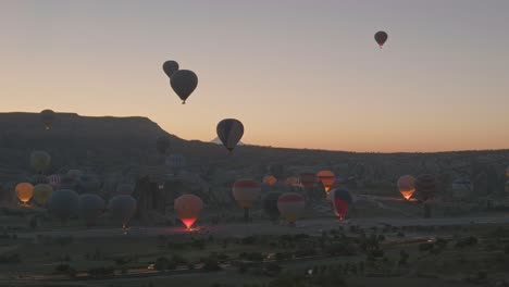 Heißluftballons-Beleuchten-Die-Startzone-Am-Frühen-Morgen-In-Der-Dunklen-Landschaft