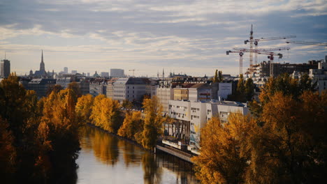 Golden-fall-colors-line-canal-river-with-buildings-and-cranes-behind-in-Spittelau-Vienna-Austria