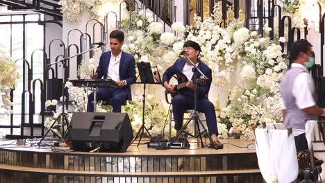 Two-wedding-singers-are-singing-and-playing-their-musical-instruments,-a-guitar-and-a-digital-drum-set-for-a-wedding-reception-in-a-hotel-in-Bangkok,-Thailand