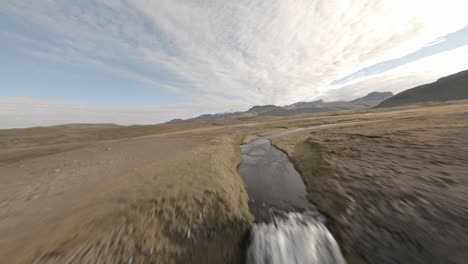 FPV-aerial-shot-that-spots-and-heads-toward-a-stream-and-climbs-a-waterfall-to-reveal-an-expansive-valley-and-mountain-range-in-Iceland