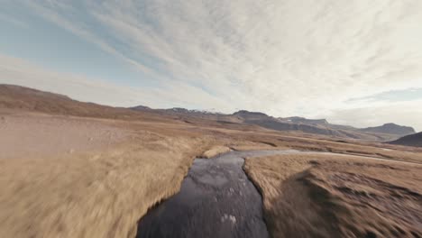 FPV-aerial-shot-that-tracks-with-a-stream-and-climbs-a-waterfall-to-reveal-an-expansive-valley-and-mountain-range-in-Iceland