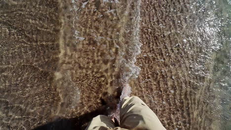 Barefoot-person-walking-on-sandy-sea-coast-with-water,-POV-view