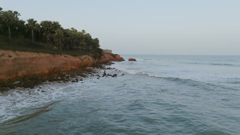 Große-Luftaufnahmen-Vor-Der-Küste-Gambias-Am-Morgen,-Die-Einen-Mann-Auf-Einem-Felsen-Zeigen,-Der-In-Den-Wellen-Fischt