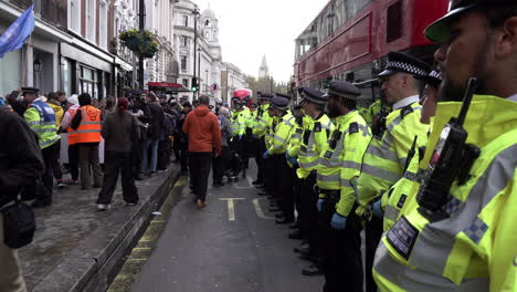 Metropolitan-police-officers-line-up-and-form-a-cordon-along-the-roadside,-to-prevent-any-protesters-from-re-entering-the-road-during-a-Just-Stop-Oil-protest