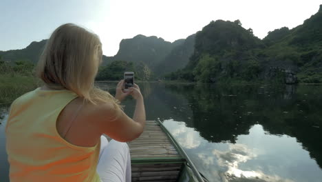 Female-tourist-taking-photos-with-cell-during-boat-in-Trang-An-Vietnam