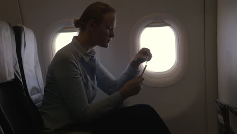 In-airplane-view-of-woman-making-payment-with-bank-card-using-smartphone-and-dongle-for-scanning-bank-card