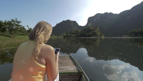 Woman-traveler-with-mobile-taking-shots-during-Trang-An-boat-tour-Vietnam