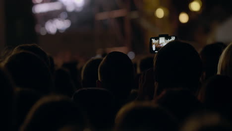 View-from-behind-of-hands-hold-camera-with-digital-display-among-people-at-rave-party-with-light