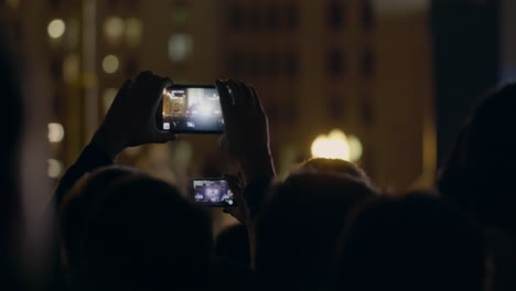View-from-behind-of-hands-hold-smartphone-among-people-at-rave-party-with-light