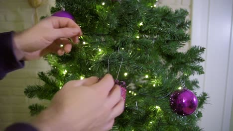 Static-shot-of-young-adult-hanging-christmas-decoration-in-the-christmas-tree-during-the-holiday-season