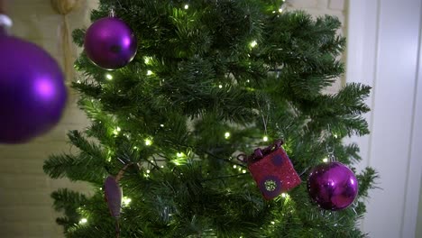 Young-adult-male-hanging-purple-decoration-in-the-christmas-tree-during-the-holiday-season