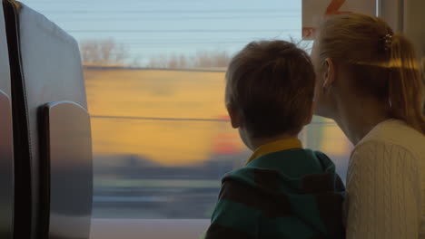 Small-boy-with-mother-sitting-against-window-in-their-rail-train-place-and-watching-outside-on-freight-trains