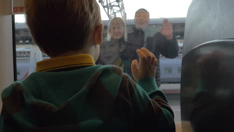 Back-view-of-boy-watching-in-window-from-rail-train-and-saying-goodbye-his-grandparents-swinging-arms