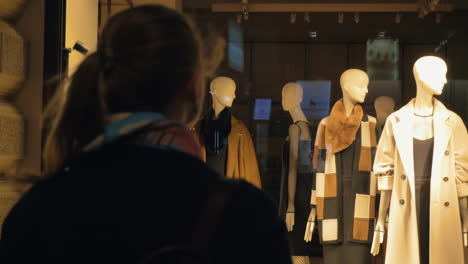 Back-view-of-woman-going-to-the-shop-window-with-female-mannequins