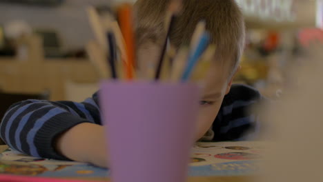 Small-boy-solves-kids-exercise-in-developing-book-for-preschool-children-unfocused-glass-with-pencils-on-the-foreground