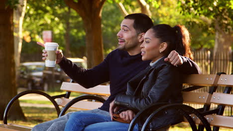 Young-Hispanic-couple-sit-talking-on-bench-in-Brooklyn-park