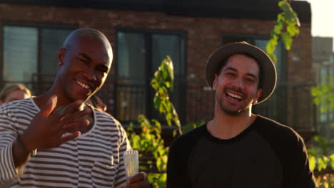 Three-male-friends-gesturing-to-camera-at-a-rooftop-party