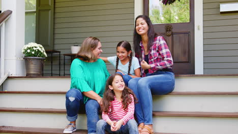 Weibliche-Mehrgenerationenfamilien-Sitzen-Auf-Stufen-Vor-Dem-Haus