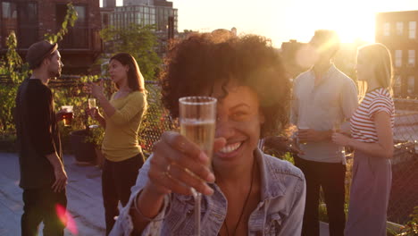 Young-black-woman-raising-a-glass-to-camera-at-rooftop-party