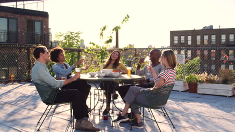 Friends-drinking-at-a-table-on-roof-terrace,-full-length
