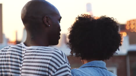 Young-black-couple-embracing-talk-on-a--rooftop,-back-view