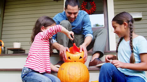 Father-And-Daughters-Carving-Halloween-Pumpkin-On-House-Steps