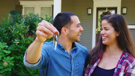 Portrait-Of-Couple-Holding-Keys-To-New-Home-On-Moving-In-Day