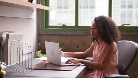 Young-black-woman-working-alone-with-laptop-in-small-office
