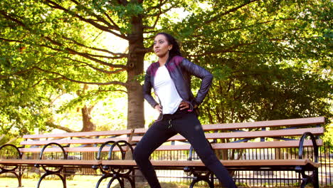 Young-black-woman-stretching-on-bench-in-a-park,-full-length