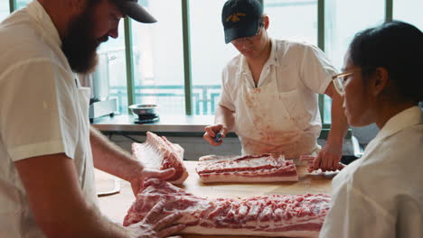 Butcher-training-colleague-to-prepare-meat-at-butcher's-shop